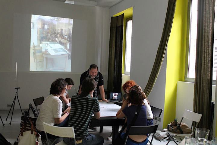 Workshop: i partecipanti discutono quanto osservato attorno a un tavolo, con una presentazione proiettata